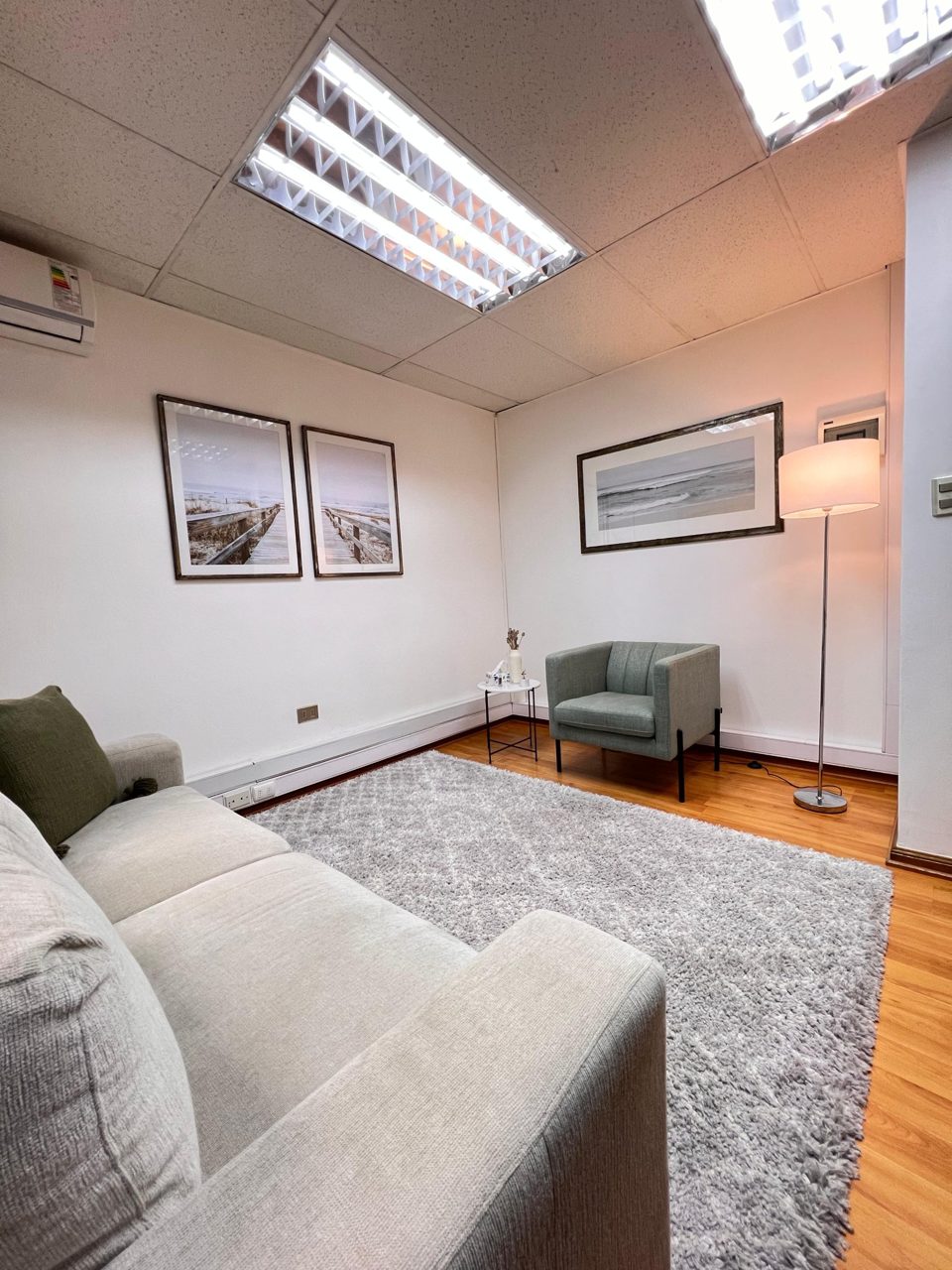 Consulta de Psincronía: un sillón verde, un sofá gris claro y una lámpara de pie, con luz suave.