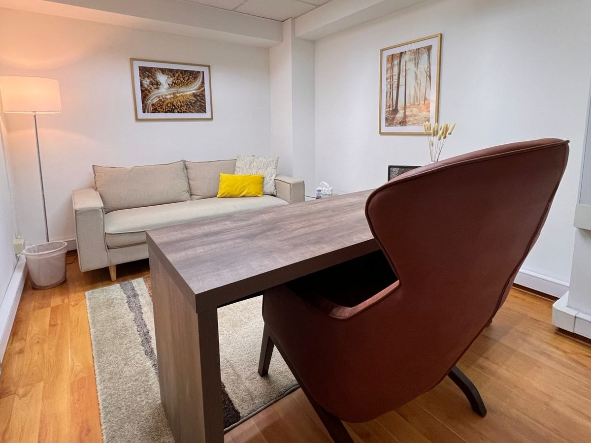 Consulta con sofá beige, cuadros de bosque, alfombra y sillón terracota.